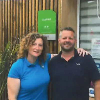 Deux adultes souriants devant panneau vert Camping